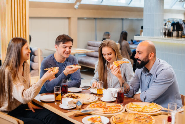 酒吧一群年轻开朗的朋友正坐在咖啡馆里聊天 吃着披萨午餐在披萨店可乐会议咖啡馆