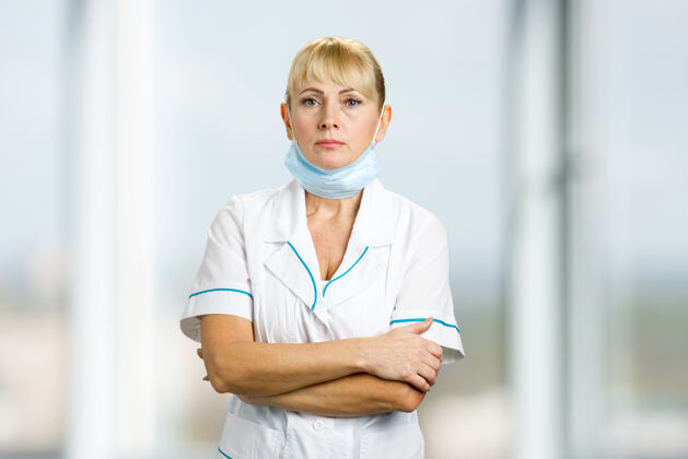 护理戴着医用面罩的护士的画像严肃的成熟医生站在下巴下面 戴着医用面罩下巴女士手