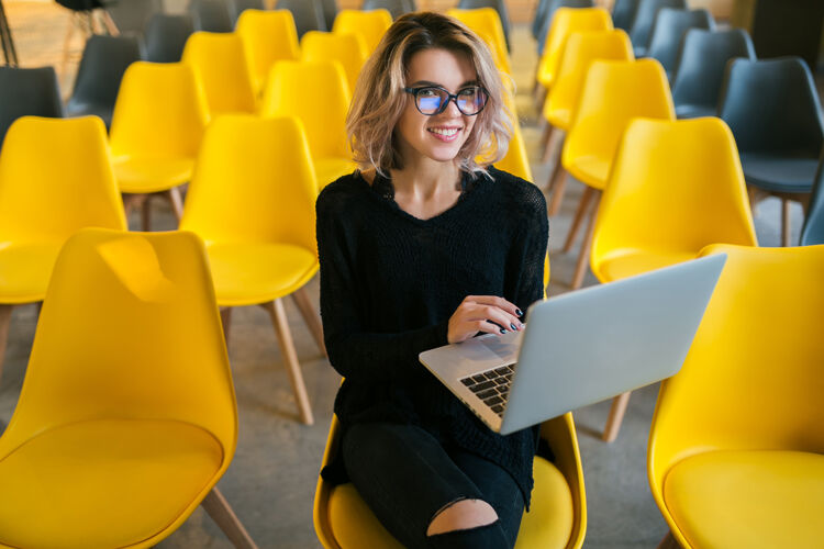 班级年轻漂亮的女士戴着眼镜坐在讲堂里用笔记本电脑工作的画像微笑漂亮妇女