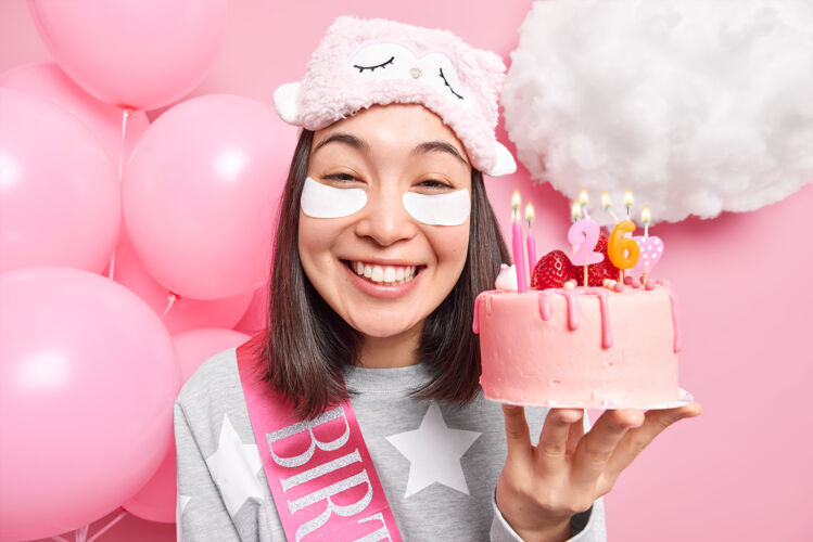心情女人笑容可掬地捧着美味的生日蛋糕在家欢庆派对上穿着休闲家装摆出粉色的姿势满意高兴亚洲