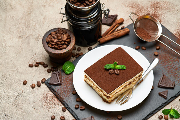 可可粉一份传统的意大利提拉米苏甜点和咖啡研磨机放在灰色的混凝土桌上传统咖啡豆饼干