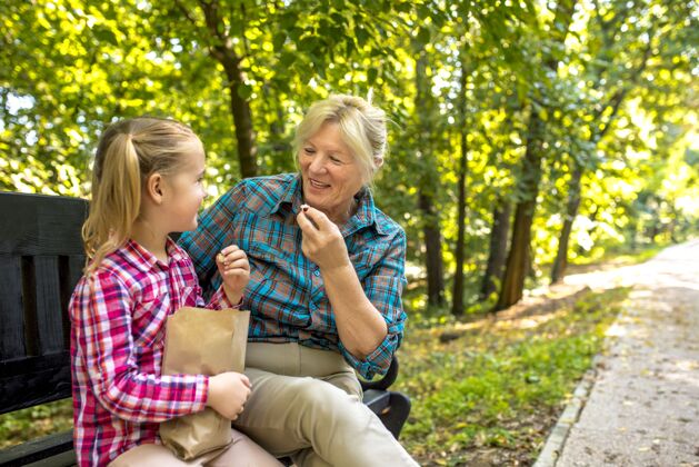 微笑微笑着的祖母坐在长椅上和她的女孙女在公园里休闲女孩长凳