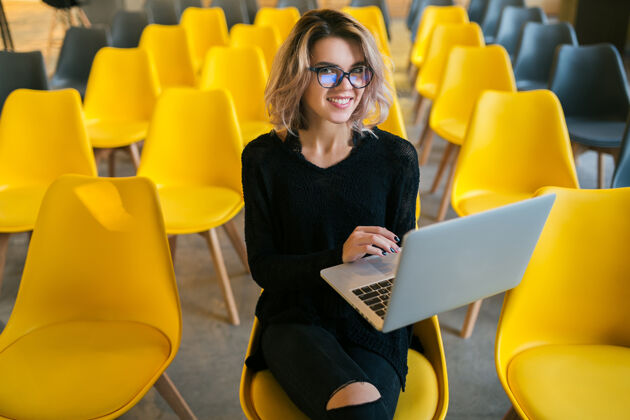 班级年轻漂亮的女士戴着眼镜坐在讲堂里用笔记本电脑工作的画像微笑漂亮妇女