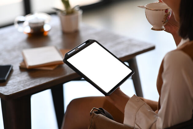 屏幕在办公室休息时喝咖啡和使用数字平板电脑的年轻女上班族的不规则镜头咖啡战略办公桌