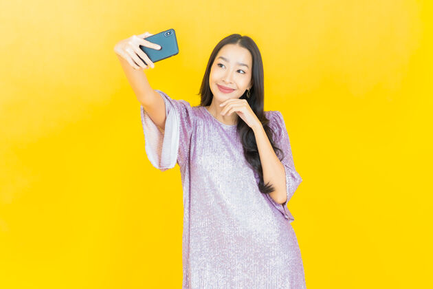 人物年轻的亚洲女人微笑着用黄色的智能手机手持设备手指