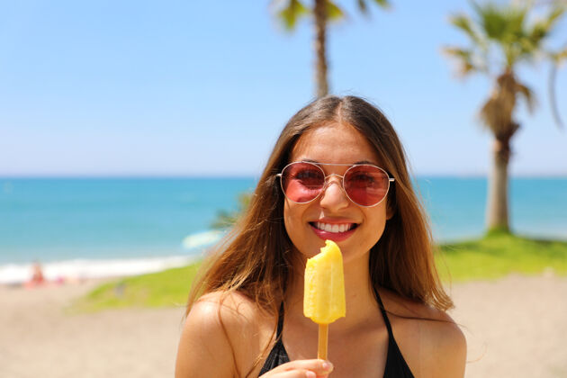 太阳镜戴着太阳镜的女人在沙滩上用棕榈树吃冰棍冰女人冰淇淋