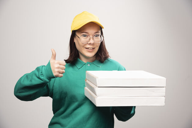女性女送货员竖起大拇指 拿着一张白色的高质量照片上的比萨饼卡片姿势芳香眼镜