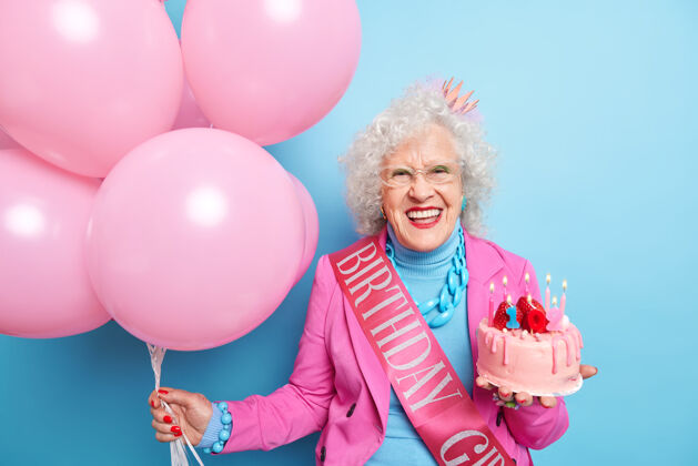 高兴快乐的老太太笑容满面露出洁白的牙齿去庆祝生日节日积极气球