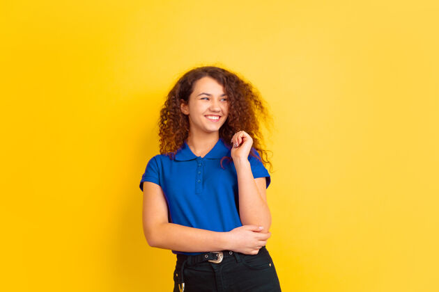 黑发微笑 欢笑黄色工作室背景上的高加索少女肖像蓝色衬衫上美丽的女性卷发模特人类情感的概念 面部表情 销售 广告空间卷发公司手