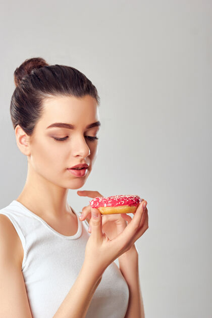 顶部一个饥饿的女孩吃甜点的特写照片孤立的黑发的女孩拿着一个粉红色的甜点尝了尝规模快速饥饿