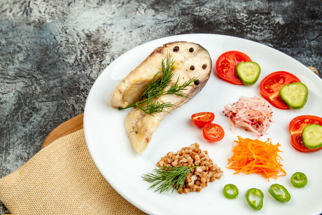 蔬菜正面近距离观看煮熟的鱼荞麦饭 绿色蔬菜放在白色盘子上 裸毛巾放在冰表面的木质砧板上午餐食物裸体