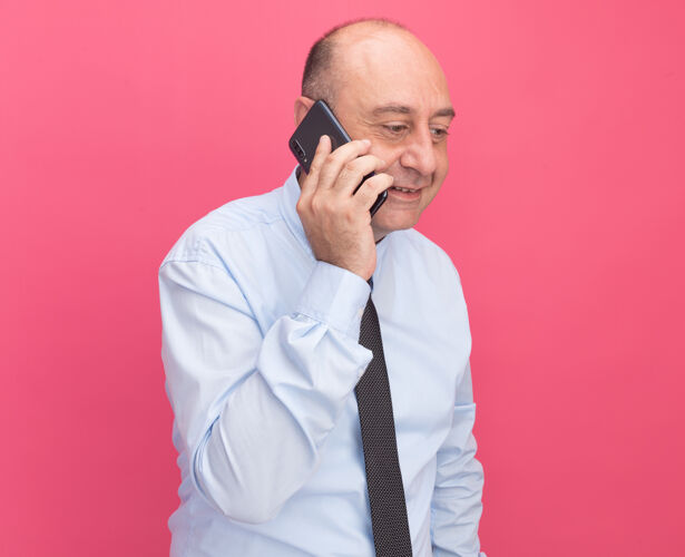 微笑微笑着低头的中年男子身穿白色t恤 打着领带 在粉红色的墙上讲电话站着人表情