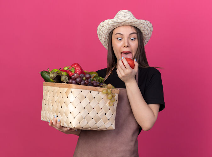 粉色兴奋漂亮的白人女园丁戴着园艺帽 伸出舌头 拿着菜篮子 看着西红柿篮子卡住了穿