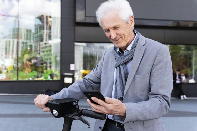 电动滑板车城里的老人用智能手机开着电动滑板车老年人城市男人