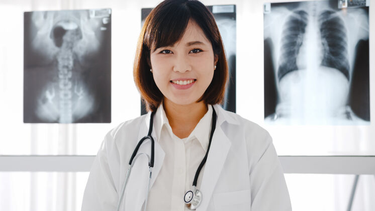韩国人自信的年轻亚洲女医生 身穿白色医疗制服 手持听诊器 看着摄像机 微笑着与健康医院的患者进行视频电话会议医生教授科学家