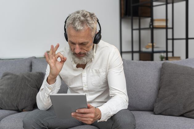 胡须家里的老人坐在沙发上用平板电脑打视频电话 戴着耳机沙发耳机内部
