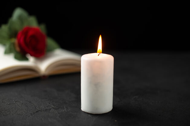 烛光打开的书和蜡烛上的黑玫瑰的正面视图葬礼火红玫瑰