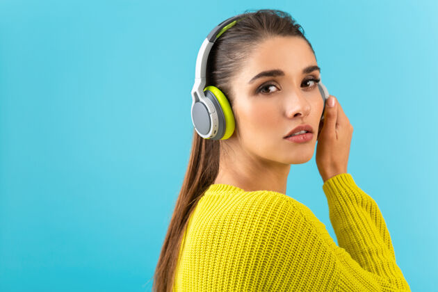 时尚迷人时尚的年轻女子戴着无线耳机听音乐快乐地穿着黄色针织毛衣五颜六色的时尚造型摆姿势欢乐音频耳机