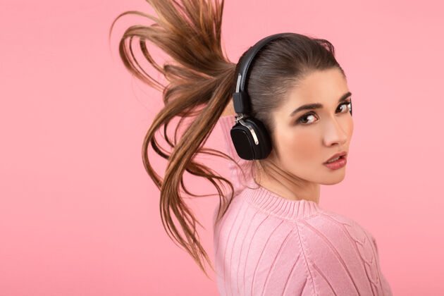 服装年轻迷人的女人戴着无线耳机听音乐穿着粉色毛衣微笑着快乐积极的心情摆在粉色背景上耳机女人女人