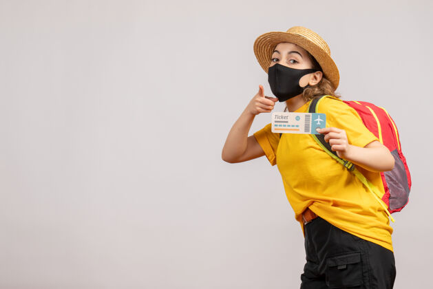 旅游正面图戴着黑色面具的年轻女子拿着旅行票指着前面度假旅游人