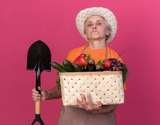 篮子自信的上了年纪的女园丁戴着园艺帽手持铁锹和菜篮子帽子抱自信