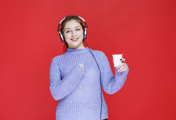 休闲戴着耳机拿着一次性咖啡的女孩女性快乐工人