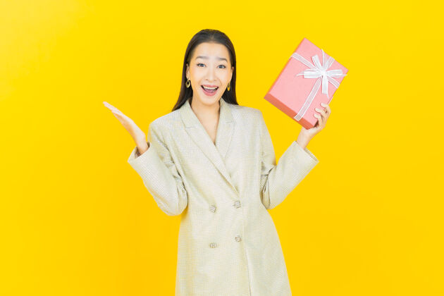 冬天肖像美丽的亚洲年轻女子微笑与红色礼品盒在彩色墙上举行礼物节日