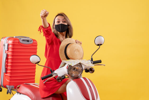 道路正面图：骑着轻便摩托车的穿着红裙子的年轻女士举手车辆旅行轻便摩托车