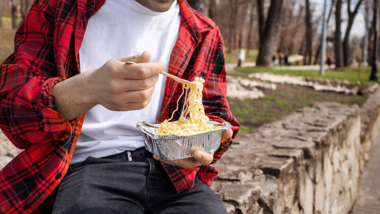 放松穿红衫的年轻人在公园里吃意大利面运动团体花园