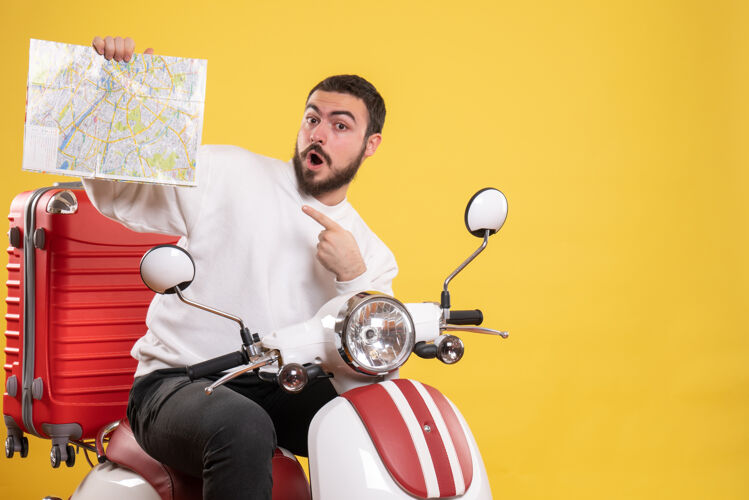 人旅行的概念与惊讶的家伙坐在摩托车上 手提箱上指着黄色地图男性地图比赛
