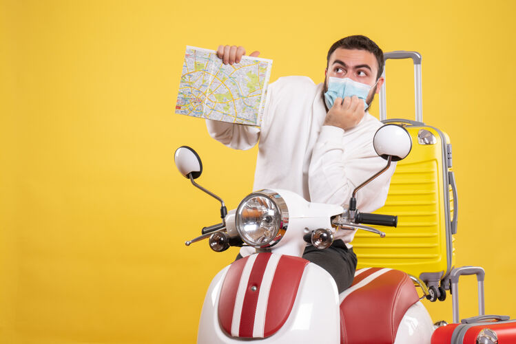 地图旅行概念的俯视图 戴着医学面罩的思考者站在摩托车旁边 黄色手提箱在上面 拿着地图运动旅行视图