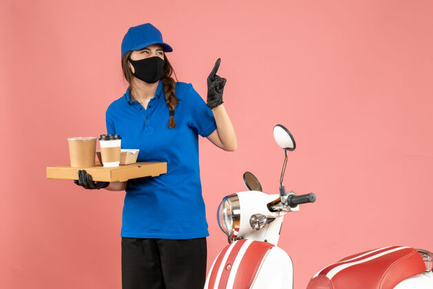 粉彩俯视图情感快递女孩戴着医用口罩手套站在摩托车旁拿着咖啡小蛋糕指着粉色背景背景男医疗