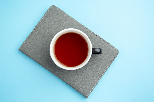 按钮一杯红茶在蓝色表面的灰色笔记本上俯瞰笔记板杯子