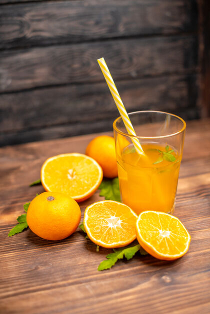 柠檬新鲜橙汁的垂直视图 在木桌的左侧有薄荷管和整个切好的橙子木材橙汁水果