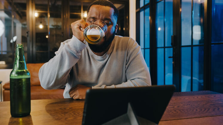 社交中年非洲裔美国男性在家中客厅通过视频通话 喝啤酒 享受快乐之夜派对活动在线庆祝活动啤酒庆祝距离