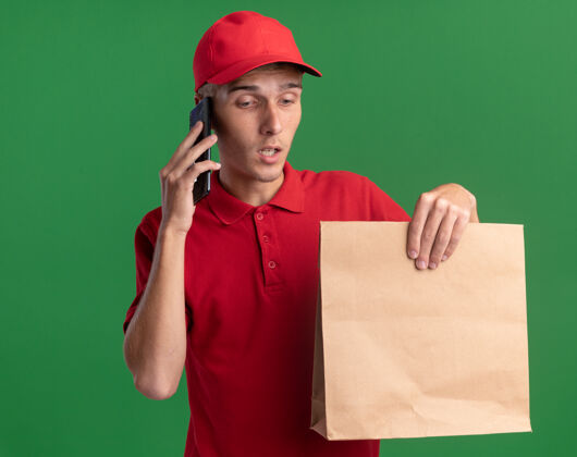 电话失望的年轻金发送货男孩拿着纸包裹 在电话里交谈持有包装送货