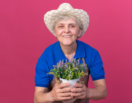 花盆微笑的上了年纪的女园丁戴着园艺帽拿着花盆手捧帽子粉色