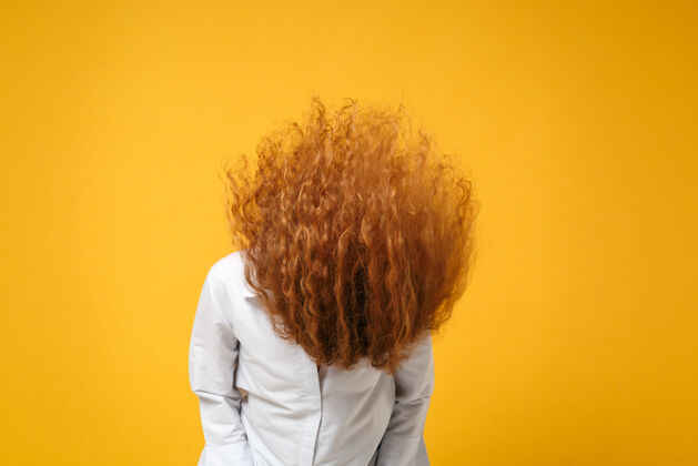 一疯狂的年轻红发女女孩穿着休闲白衬衫在黄橙色的墙上摆出孤立的姿势白种人脸女人