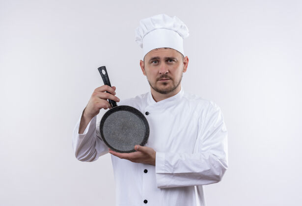 烹饪自信的年轻帅哥厨师身着厨师制服 手拿煎锅孤立在白墙上手持薯条厨师