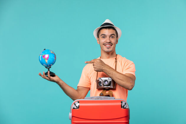 成人正面图：度假中的男性手持小地球仪 微笑着面对蓝色旅行举行假期