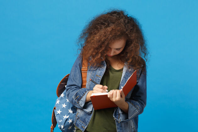 截止日期年轻的非洲裔美国少女 穿着牛仔服 背着书包 孤零零地站在蓝色的墙上学校人悲伤