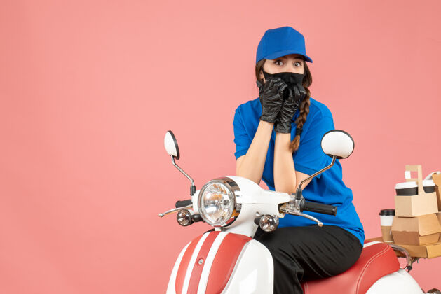 摩托车俯视图：戴着医用面罩和手套的快递员女孩坐在滑板车上 用粉彩桃子传递订单桃面具粉彩