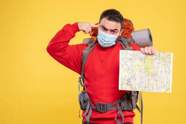 背包俯视图是一个情绪化 体贴的旅行者 他戴着医用面罩 背着黄色背景的地图人物成人医学