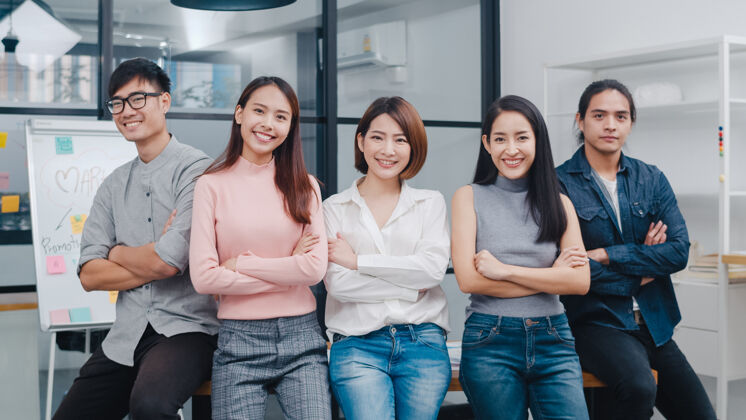 小型一群亚洲年轻创意人士穿着时髦的休闲服 微笑着双臂交叉在创意办公场所市场营销高管团结
