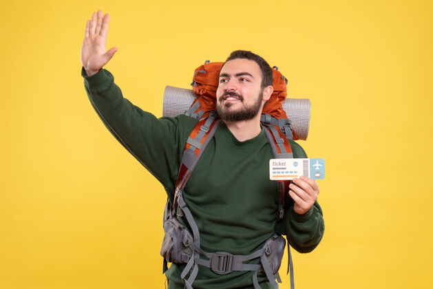 帅哥黄色背景下 背着背包和出示车票的年轻笑脸旅行小伙的正视图票黄色背包