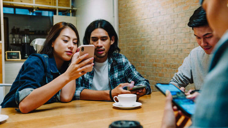 亚洲一群快乐的亚洲年轻朋友 一起坐在咖啡馆里玩得开心 一起使用智能手机团队互联网办公室