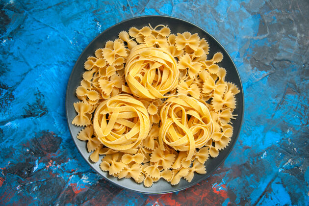 烹饪在蓝色背景上的黑色盘子上用意大利面准备晚餐的俯视图意大利面背景意大利面