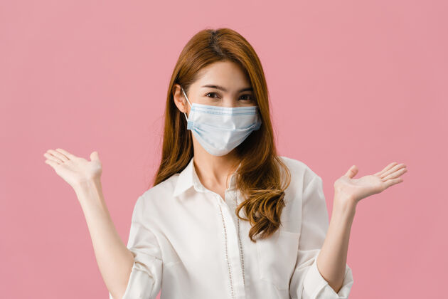 感染年轻的亚洲女孩戴着医用口罩显示和平的迹象 穿着休闲的衣服 看着隔离在粉红色背景上的相机鼓励疾病病人女士