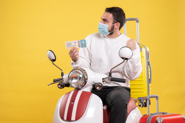 人旅行概念的俯视图 戴着医用面罩的年轻好奇者坐在摩托车上 黄色手提箱放在上面 手里拿着车票面具制服上衣