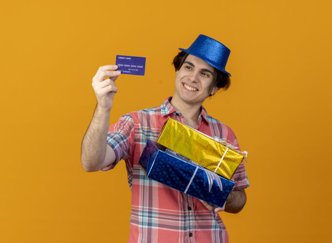 蓝色面带微笑的白人帅哥戴着蓝色派对帽拿着礼盒 看着信用卡男人聚会复制